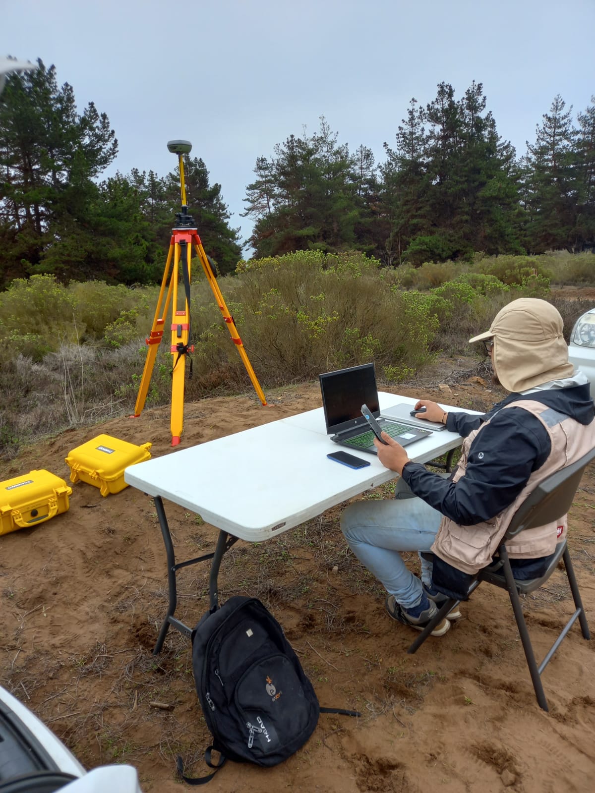 Profesional procesando los datos topográficos en un notebook en terreno, con la estación base GNSS instalada al fondo